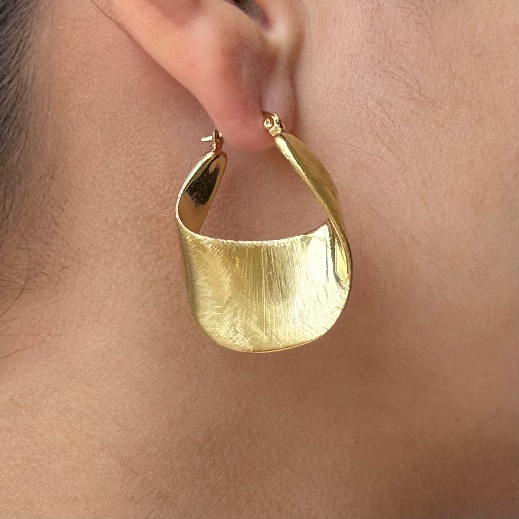 A close-up of a person's ear wearing a large, textured Wavy Hoop Earrings with a curved, leaf-like shape.