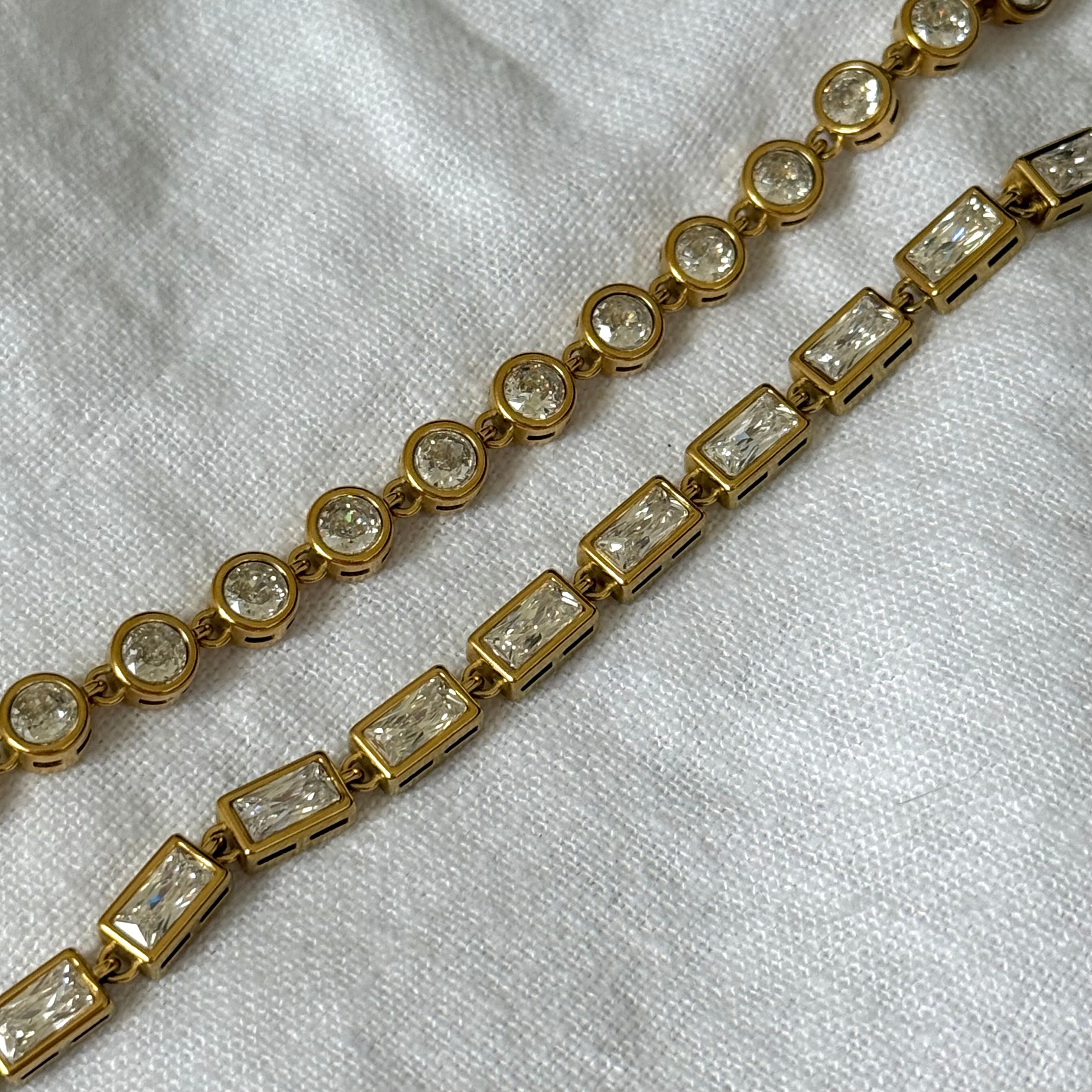 A close-up of a gold-toned tennis bracelet with alternating round and rectangular zircon stones, laid on a white textured fabric background.