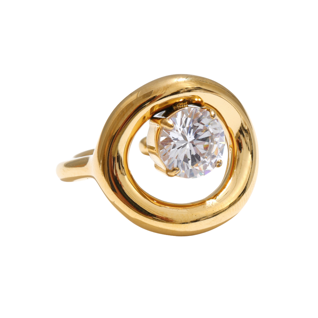 A gold Orbit Ring featuring a large, round-cut clear zircon in a prong setting, surrounded by an open, swirling oval design on a plain white background.