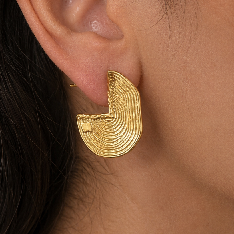 A close-up of a person's ear wearing a textured gold crescent-shaped hoop earring.