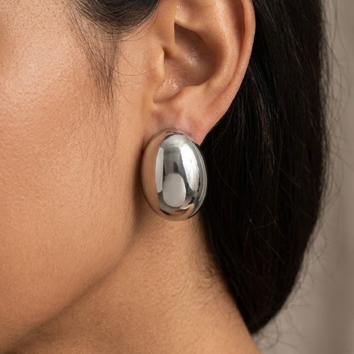 A close-up of a woman's ear wearing a large, polished silver dome earring.