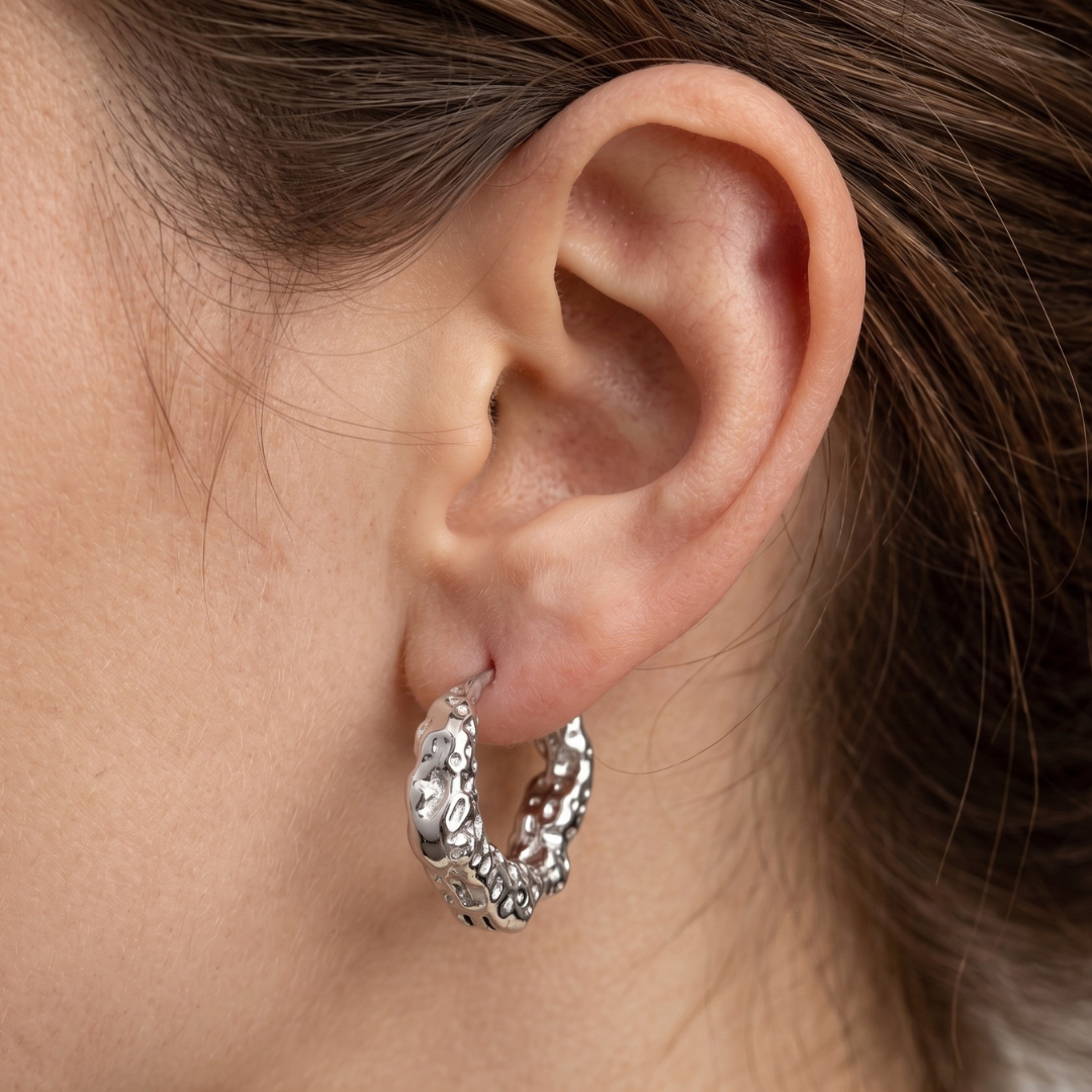A close-up of a person's ear wearing a textured silver hoop earring.
